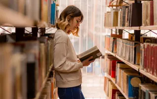 Studentin wendet an einem Buch in der Bibliothek die Lesetechnik SQ3R Methode an