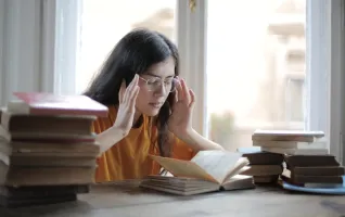 Eine junge Frau, die beim Lesen und Lernen inmitten von Büchern erschöpft ist
