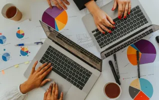 Draufsicht auf ein Team, das in einer Marketing- und Vertriebsbesprechung mithilfe von Laptops Grafiken und Diagramme analysiert