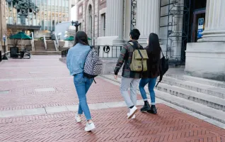 Eine Gruppe junger Studenten geht mit Rucksäcken auf einem Weg über den Universitätscampus
