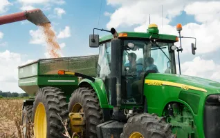 Ein grüner Traktor erntet Feldfrüchte auf einem sonnigen Feld und demonstriert damit die moderne Landwirtschaft