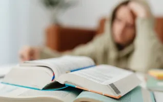Verschwommenes Bild eines Schülers, der mit offenen Büchern an einem Schreibtisch sitzt und lernt – ein Zeichen für eine Lernblockade