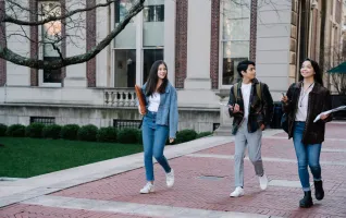 Group of young students walking on campus sidewalk on a bright day, showcasing casual university life.
