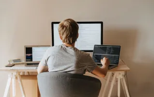 Teen programming with multiple laptops in a modern workspace.