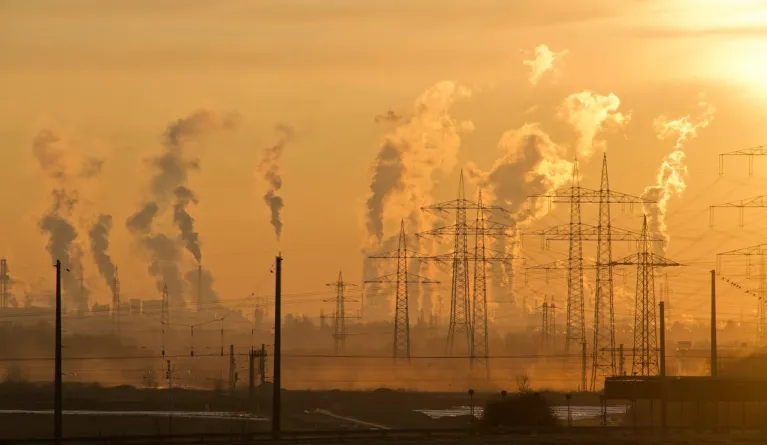 Strommasten während der goldenen Stunde mit CO2-Emissionen im Hintergrund