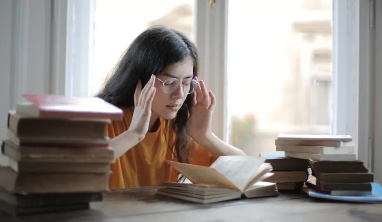 Eine junge Frau, die beim Lesen und Lernen inmitten von Büchern erschöpft ist