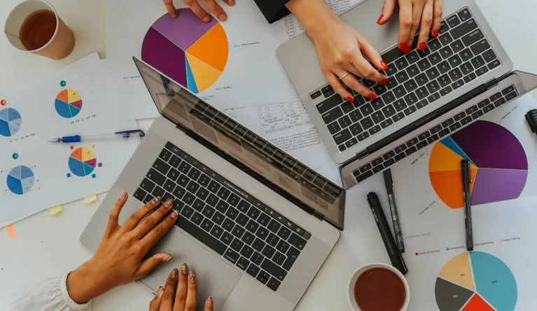 Draufsicht auf ein Team, das in einer Marketing- und Vertriebsbesprechung mithilfe von Laptops Grafiken und Diagramme analysiert