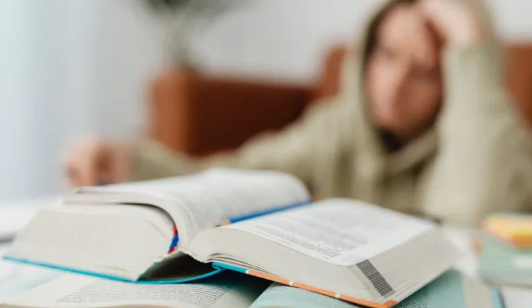 Verschwommenes Bild eines Schülers, der mit offenen Büchern an einem Schreibtisch sitzt und lernt – ein Zeichen für eine Lernblockade